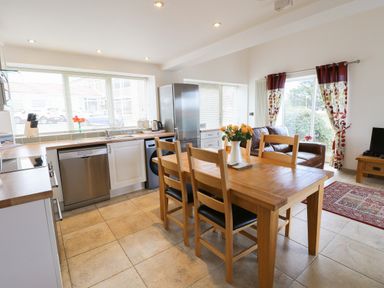 A kitchen with wooden dining table and chairs next to a living area with leather sofa and television at Mallard Cottage in Whitby