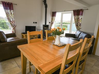 A dining area with a wooden table and chairs next to a sitting area with leather sofas and a television at Mallard Cottage in Whitby