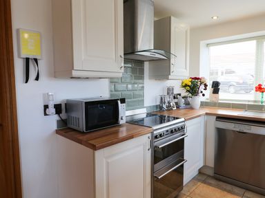 A kitchen with white cabinets a microwave stove dishwasher and flowers on the counter at Mallard Cottage in Whitby