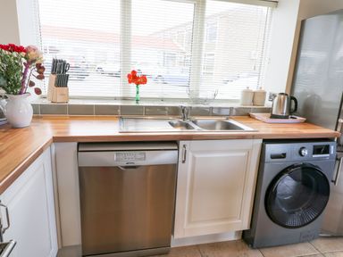 A kitchen counter with a sink dishwasher washing machine kettle and flowers at Mallard Cottage in Whitby