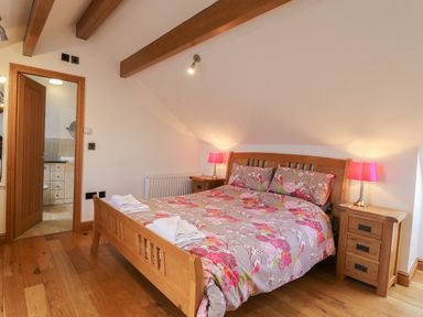 A bedroom with a wooden double bed floral bedding bedside tables with lamps and an open door to an en suite bathroom at Mallard Cottage in Whitby