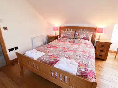A bedroom with a wooden bed and side tables with lamps and folded towels at Mallard Cottage in Whitby