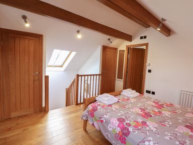 A bedroom with wooden doors wooden ceiling beams a bed with floral bedding and a skylight window at Mallard Cottage in Whitby