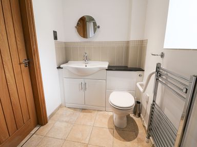 A bathroom with a wooden door a white sink vanity a toilet a round mirror and a heated metal towel rack at Mallard Cottage in Whitby