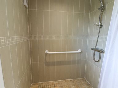 A tiled walk-in shower with a white grab bar and a handheld showerhead at Mallard Cottage in Whitby