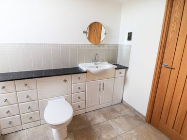 A bathroom with a toilet a sink with cabinets and a round mirror above the sink at Mallard Cottage in Whitby