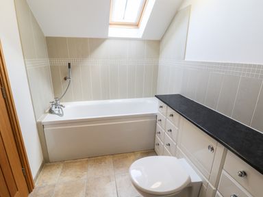A bathroom with a bathtub toilet and cabinets under a skylight window at Mallard Cottage Whitby
