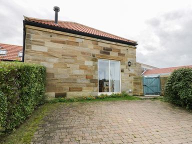 A stone house with a tiled roof and sliding glass door next to a blue gate with bushes on either side at Mallard Cottage in Whitby
