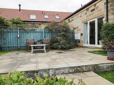 A patio area with two wooden chairs a white table blue fence and plants at Mallard Cottage in Whitby