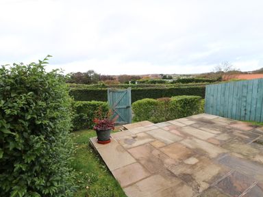 A garden area with a tiled patio a blue wooden gate green bushes and a potted plant at Mallard Cottage in Whitby