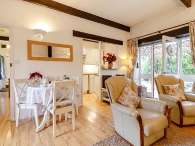 A dining area with a round table and chairs next to two armchairs near a glass door leading outside at Wagtail Cottage in East Taphouse