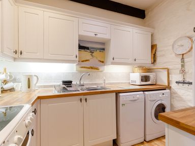 A kitchen with white cabinets a sink a microwave a kettle a washing machine and a dishwasher at Wagtail Cottage in East Taphouse