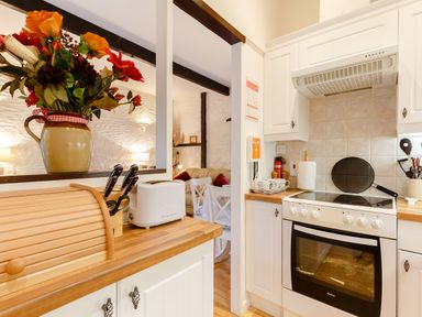 A kitchen with white cabinets a stove a toaster and a bread box with flowers on the counter at Wagtail Cottage in East Taphouse