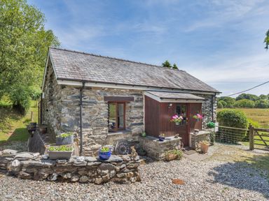 A stone cottage with flower pots on a low wall and a gravel pathway at Bwythyn Y Wennol in Nantmor near Beddgelert 