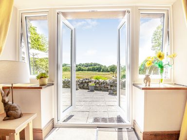 A room with open glass doors leading to a stone patio and field beyond at Bwythyn Y Wennol in Nantmor near Beddgelert