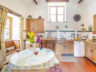 A kitchen with wooden cabinets a round table with a vase of flowers and four glasses with red drink at Bwythyn Y Wennol in Nantmor near Beddgelert 