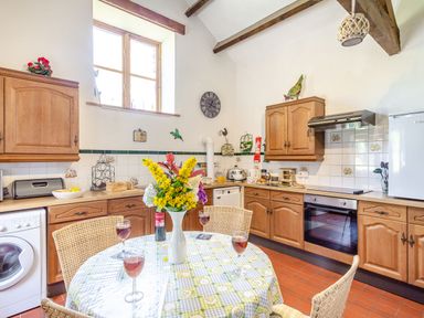 A kitchen with wooden cabinets a round table with a floral vase and wine glasses at Bwythyn Y Wennol in Nantmor near Beddgelert