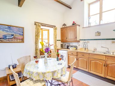 A kitchen with wooden cabinets a round table set for four with drinks flowers and a window at Bwythyn Y Wennol in Nantmor near Beddgelert 