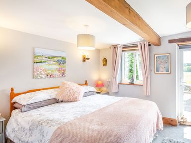 A bedroom with a double bed a pink blanket and a painting on the wall at Bwythyn Y Wennol in Nantmor near Beddgelert 