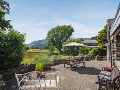 An outdoor patio with benches and a table under an umbrella overlooking a garden and hills at Bwythyn Y Wennol in Nantmor near Beddgelert 