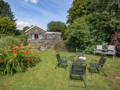 A garden with outdoor seating and a stone house in the background at Bwythyn Y Wennol in Nantmor near Beddgelert