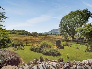 A garden with a flower bed and outdoor table with chairs overlooking fields and hills at Bwthyn Y Wennol in Nantmor near Beddgelert