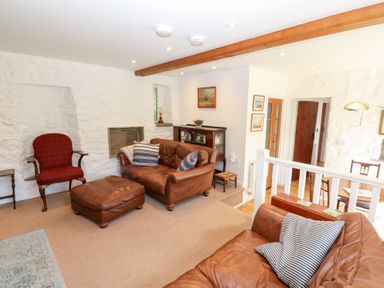 A living room with leather sofas, a red armchair, wooden furniture, and stone walls at Farrier's Cottage in Garsdale