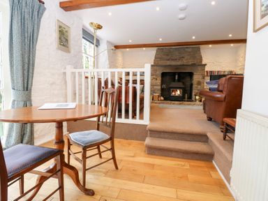 A dining area with a round wooden table and two chairs next to a step leading to a sitting room with a stone fireplace and leather sofas at Farrier's Cottage in Garsdale