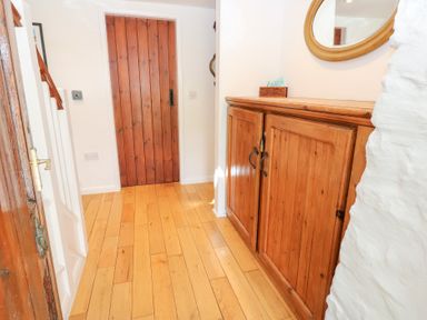 A hallway with a wooden floor wooden door wooden cabinet and white walls at Farrier's Cottage in Garsdale