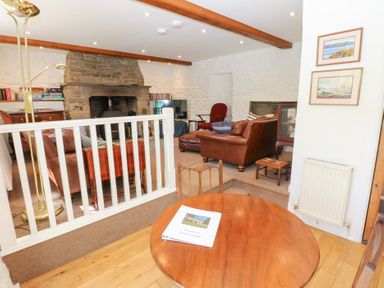 A living room with brown leather sofas a stone fireplace and a wooden table at Farriers Cottage in Garsdale