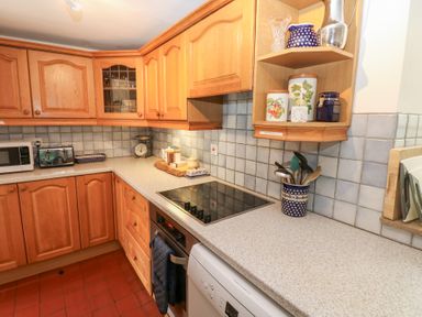 A kitchen with wooden cabinets a stovetop an oven a microwave a toaster various canisters and kitchen utensils on the countertop at Farrier's Cottage in Garsdale