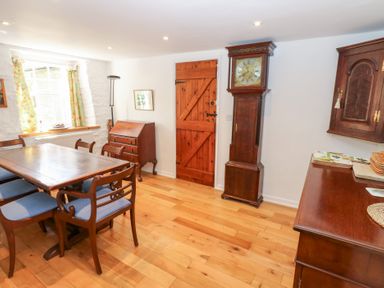 A dining room with wooden table and chairs a grandfather clock and wooden cabinets at Farrier's Cottage in Garsdale