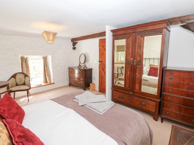 A bedroom with a bed chairs wooden wardrobe and dressers at Farrier's Cottage in Garsdale