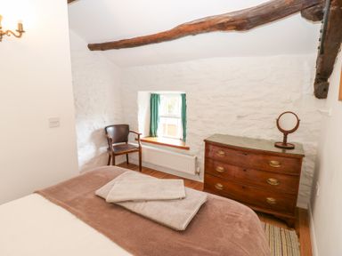 A bedroom with a bed towel on it a wooden chair under a window and a wooden dresser with a mirror at Farrier's Cottage in Garsdale