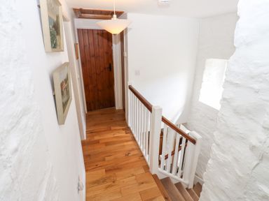 A hallway with wooden floor leading to a wooden door and stairs with white railing at Farrier's Cottage in Garsdale