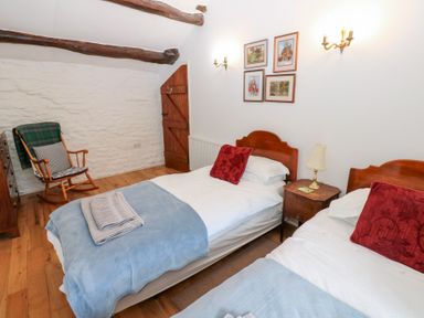 A bedroom with two single beds a wooden rocking chair and a wooden door at Farrier's Cottage in Garsdale