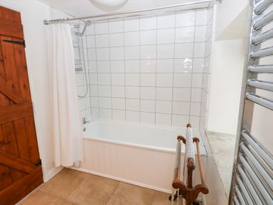 A bathroom with a bathtub white tiled walls a shower curtain wooden door and a towel rack at Farrier's Cottage in Garsdale