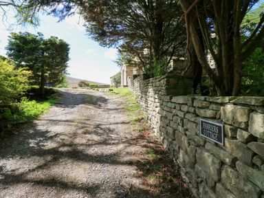 A gravel driveway with trees and a stone wall with a sign reading Farriers Cottage at Farriers Cottage in Garsdale