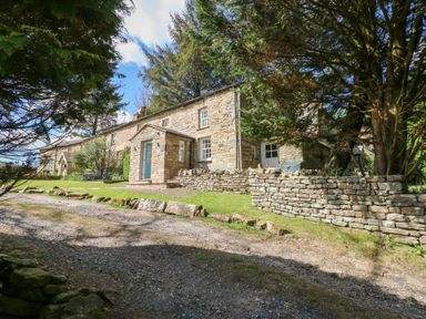 Stone house with green door and gravel path surrounded by trees and stone walls at Farrier's Cottage in Garsdale
