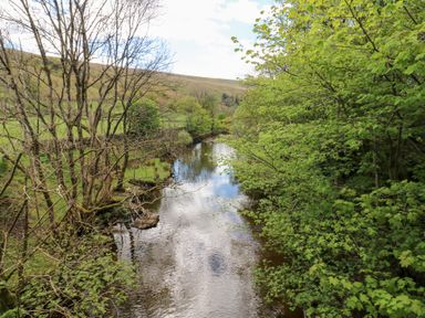 A river flowing through a landscape with bare and leafy trees at Farrier's Cottage in Garsdale