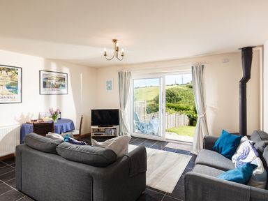 A living room with two gray sofas a dining table with chairs a TV and sliding glass doors leading outside at Nectan in Mevagissey