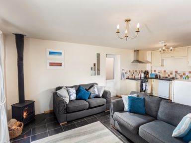 A living room with two gray sofas a wood stove and an adjoining kitchen at Nectan in Mevagissey
