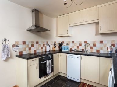A kitchen with light wood cabinets a black countertop tiled backsplash an oven dishwasher and a blue toaster at Nectan in Mevagissey
