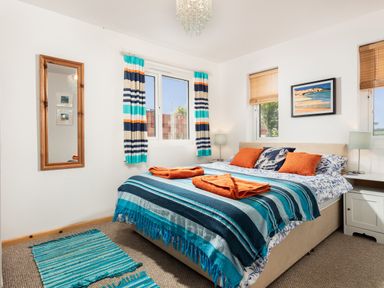 A bedroom with a bed with striped blue and teal blanket and orange towels at Nectan in Mevagissey