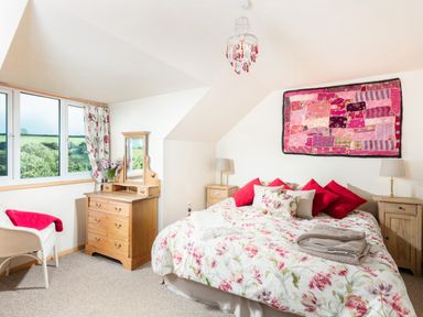 A bedroom with a floral bedspread red pillows wooden dressers and a wall hanging at Nectan in Mevagissey