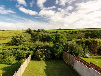A fenced garden with bushes and a lawn with hills and trees in the background at Nectan in Mevagissey