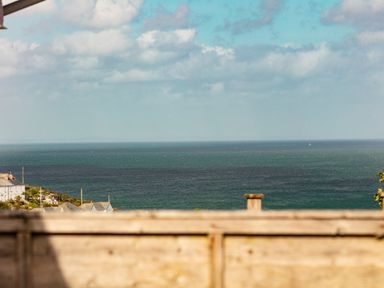 A view of the sea with houses on the left and a wooden fence in the foreground at Nectan in Mevagissey