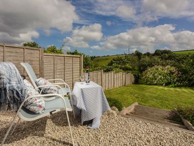 An outdoor seating area with two chairs and a table with a bottle and glasses next to a grassy garden at Nectan in Mevagissey