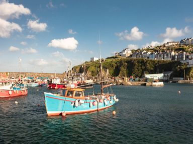 A harbor with several docked fishing boats and houses on a hill by the water at Nectan in Mevagissey
