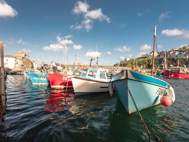 A harbor with multiple fishing boats docked with buildings and hills in the background at Nectan in Mevagissey